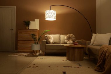 Şık oturma odasının içinde rahat koltuklar, sehpa ve gece lamba parlıyor.