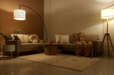 Şık oturma odasının içinde rahat koltuklar, sehpa ve akşam lambaları var.