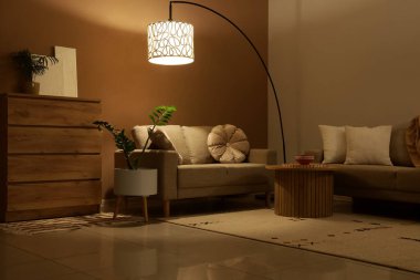 Şık oturma odasının içinde rahat koltuklar, sehpa ve gece lamba parlıyor.