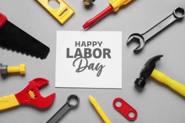 Oyuncak yapım araçları ve gri arkaplanda Mutlu Günler yazılı tebrik kartı. İşçi Bayramı kutlamaları