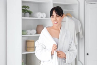 Evde bornozlu genç bir kadın var.