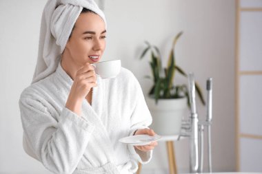 Evde duştan sonra yumuşak bornozlu genç bir kadın bir fincan kahveyle