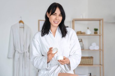 Evde bir kavanoz kremalı, yumuşak bornozlu genç bir kadın var.