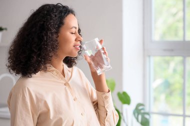 Genç Afro-Amerikalı kadın mutfakta su içiyor.