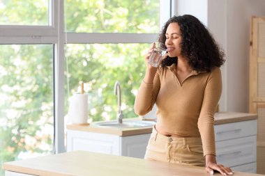 Genç Afro-Amerikalı kadın mutfakta su içiyor.