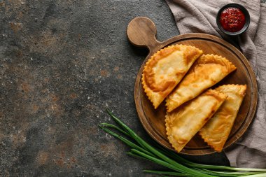 Lezzetli chebureks, sos ve siyah grunge masasında taze yeşil soğan.