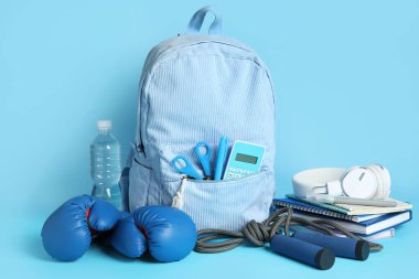 Sırt çantası, okul malzemeleri ve mavi arka planda spor malzemeleri.