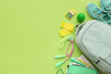 Sırt çantalı kompozisyon, okul malzemeleri ve yeşil arka planda spor malzemeleri.