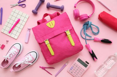 Sırt çantalı kompozisyon, okul malzemeleri ve pembe arka planda spor malzemeleri.