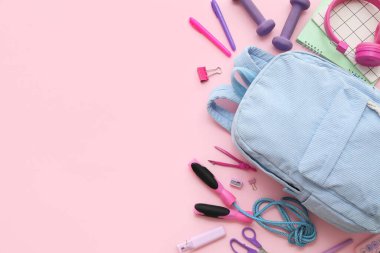 Sırt çantalı kompozisyon, okul malzemeleri ve pembe arka planda spor malzemeleri.