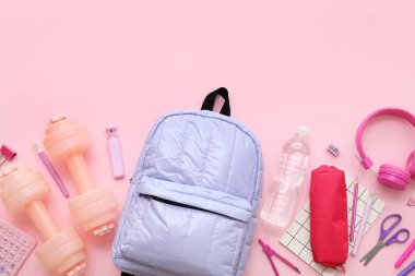 Sırt çantalı kompozisyon, okul malzemeleri ve pembe arka planda spor malzemeleri.