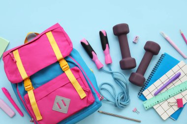 Sırt çantalı kompozisyon, okul malzemeleri ve mavi arka planda spor malzemeleri.