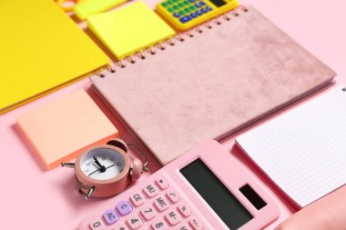 Pembe arka planda farklı okul kırtasiyesi, alarm saati ve hesap makinesine sahip kompozisyon, yakın plan