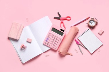 Pembe zemin üzerinde farklı okul kırtasiyesi, alarm saati ve hesap makinesi olan kompozisyon