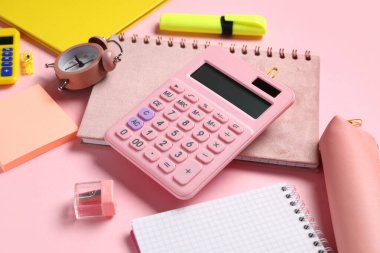 Pembe arka planda farklı okul kırtasiyesi, alarm saati ve hesap makinesine sahip kompozisyon, yakın plan