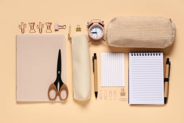 Bej arkaplan üzerinde farklı okul kırtasiyesi ve alarm saati olan kompozisyon, yakın plan