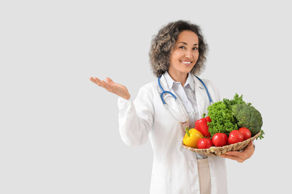 Зрелая женщина-диетолог со здоровыми овощами на светлом фоне