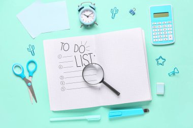 Boş defter, çalar saat, büyüteç ve turkuaz arka planda okul malzemeleri içeren kompozisyon, yakın plan