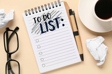Boş yapılacaklar listesi olan defter, kahve, buruşmuş kağıt, gözlük ve bej arka planda kalem
