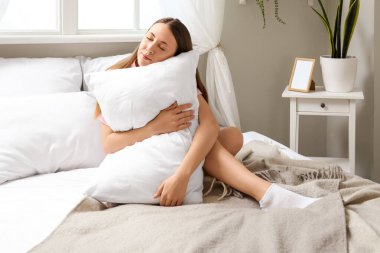 Yumuşak yastıklı güzel bir kadın yatakta oturuyor.