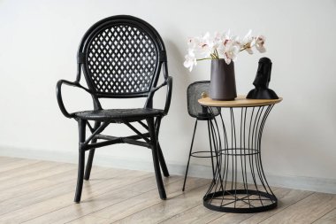 Sehpanın üzerinde güzel orkide çiçekleri ve beyaz duvarın yanında siyah bir koltuk olan vazo.