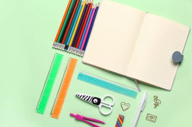 Yeşil arka planda farklı kırtasiye malzemesi içeren defter