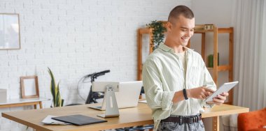 Genç adam ofiste tablet bilgisayarla çalışıyor.