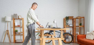 Genç adam ofisteki koşu bandında dizüstü bilgisayarla çalışıyor.