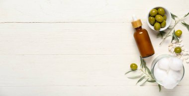 Beyaz ahşap zemin üzerinde yeşil zeytin ve pamuk topları, doğal yağ şişesi.