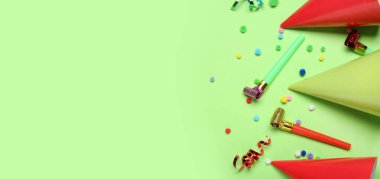 Yeşil arkaplanda parti şapkaları, düdükler ve konfetiler.