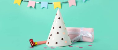 Parti şapkası, düdük, hediye kutusu ve turkuaz arka planda çelenk.