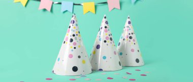 Parti şapkaları, konfeti ve turkuaz arka planda kağıt çelenkler.