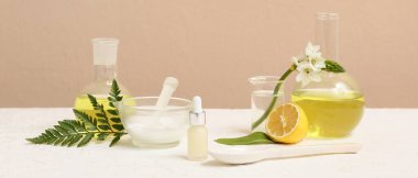 Bej duvarın yanındaki beyaz masada doğal kozmetik ürünleri hazırlamak için malzemeler ve numunelerle dolu laboratuvar vitrinleri.