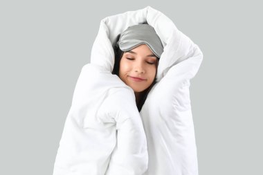 Gri arka planda uyuyan yumuşak battaniyeye sarılı güzel genç bir kadın.