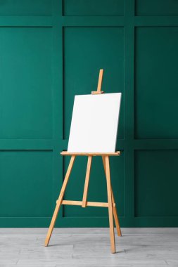 Yeşil duvarın yanında boş tuval olan tahta sehpa.