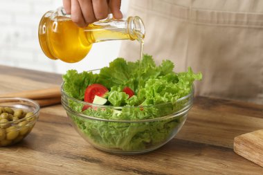 Mutfaktaki masada lezzetli salata ile zeytinyağı ekleyen bir kadın.