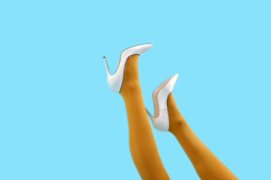 Mavi arka planda şık beyaz topuklu genç kadın bacakları.