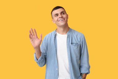 Sarı arka planda el sallayan yakışıklı genç adam.