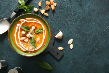 Koyu arkaplanda tohumlu ve fesleğenli balkabağı kremalı çorba.