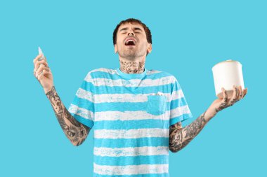 Mavi arka planda hapşıran burun damlası ve dokuları olan alerjik genç bir adam.