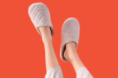 Turuncu arka planda yumuşak terlikler giyen kadın bacakları.