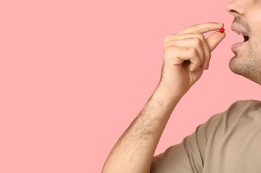 Genç adam pembe arka planda A vitamini hapı alıyor, yakın plan.