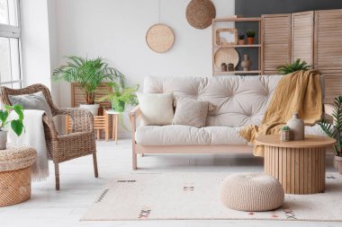 Işıl ışıl oturma odasının içinde rahat beyaz kanepe, sehpa ve hasır koltuk.