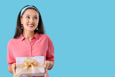 Mavi arka planda hediye kutusu olan güzel bir Asyalı kadın.