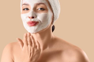 Uygulamalı yüz maskeli güzel bir kadın. Bej arka planda öpüşüyor. Yakın plan.