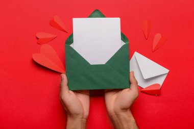 Zarflı erkek eller, boş kartlar ve kırmızı arka planda kağıt kalpler. Sevgililer Günü kutlaması