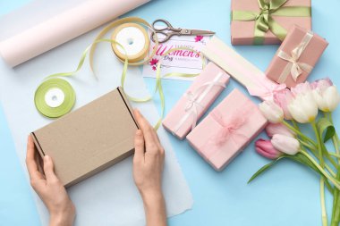 Hediye kutularıyla kadın elleri, ambalaj kağıtları ve mavi arka planda güzel laleler. Uluslararası Kadınlar Günü