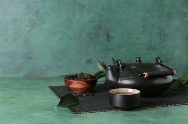 Çaydanlıklı bambu hasırı, fincan ve yeşil grunge arka planda bir kase kuru çay yaprağı.