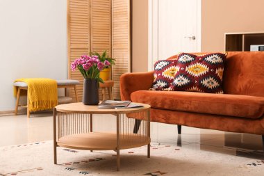 Kahverengi kanepesi ve kahve masasında güzel laleleri olan şık bir oturma odası.