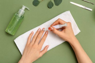 Tırnaklara, okaliptüs dalına ve yeşil arka planda havluya tırnak yağı süren kadın eller.